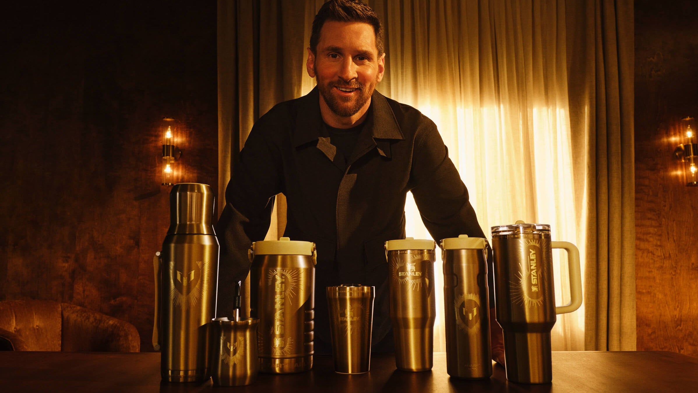 Messi standing behind a display of metallic tumblers in a warm-lit room.