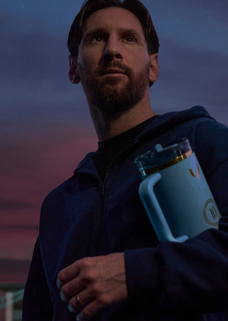 Messi holding a blue mug against a dark sky
