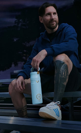 Messi sitting outdoors holding a blue water bottle with a logo.