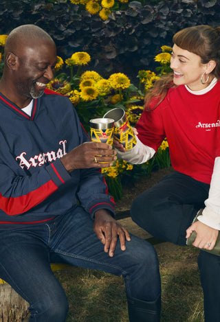 Two people sitting outdoors with Arsenal-themed clothing, holding drinks.