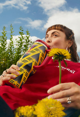 Person holding a mug with a pattern and a yellow flower against a blue sky.
