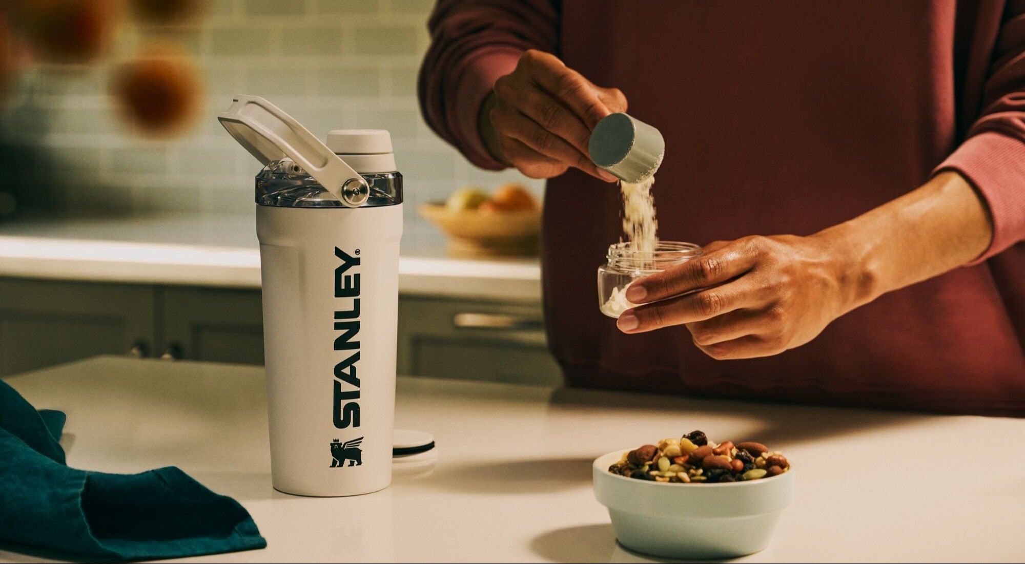 Person pouring liquid into a jar next to a Stanley tumbler in a kitchen setting.
