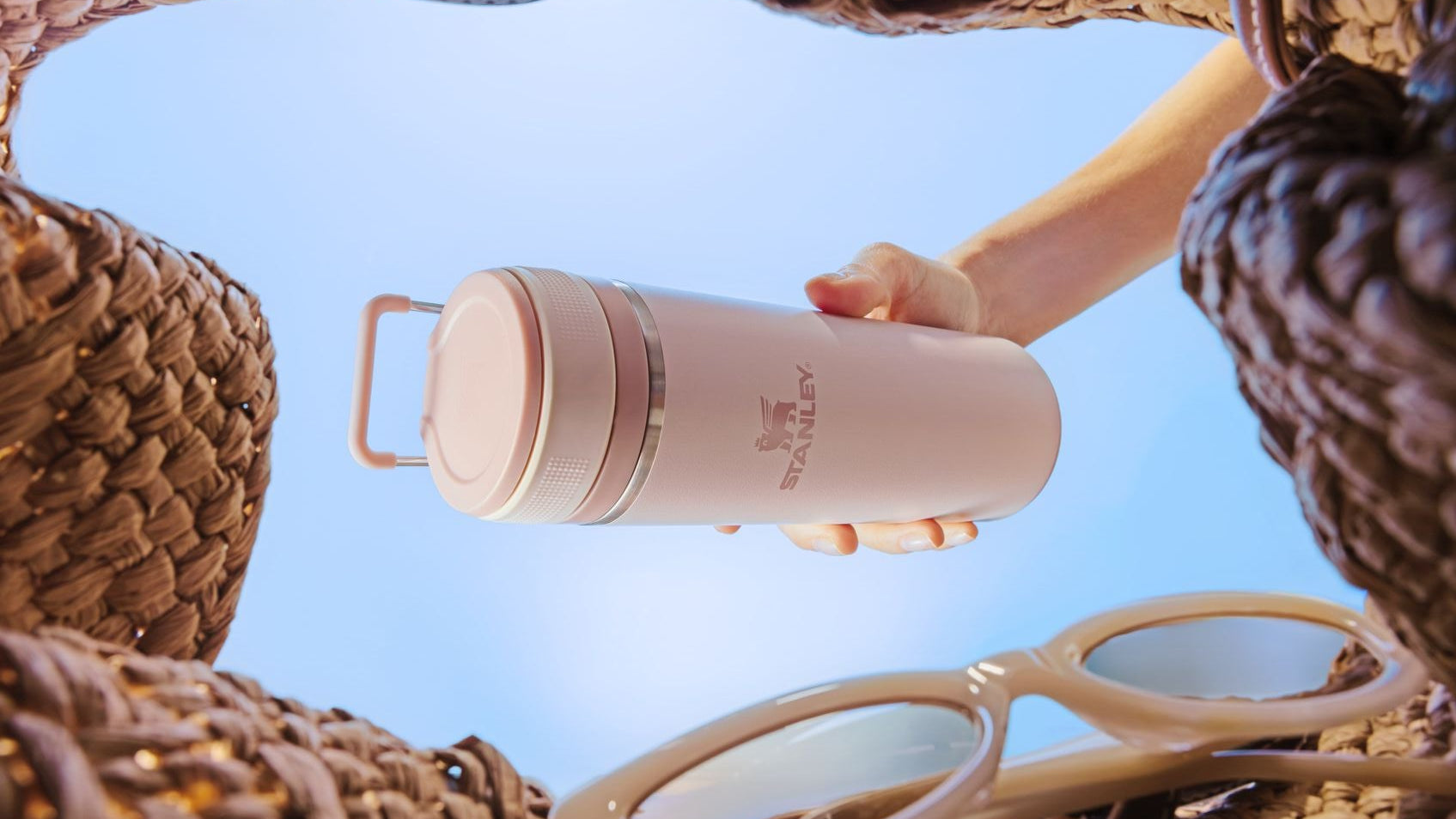 Person holding a pink travel mug with sunglasses on a textured surface
