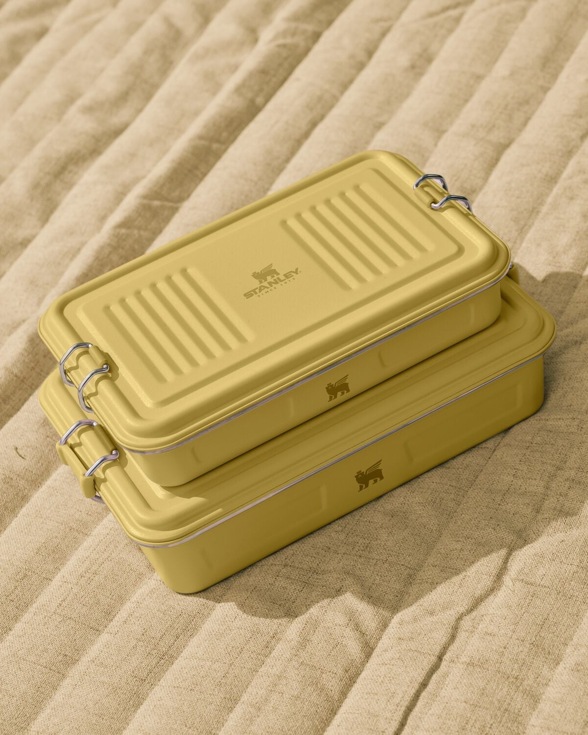 Two yellow metal lunch boxes stacked on a beige textured surface