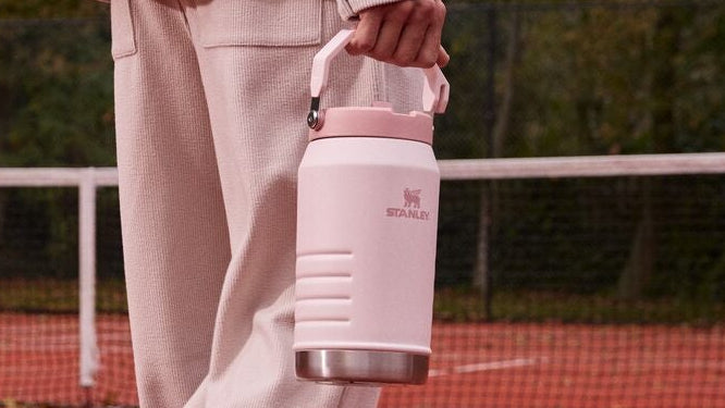 Person in light pink outfit holding a water bottle on a tennis court